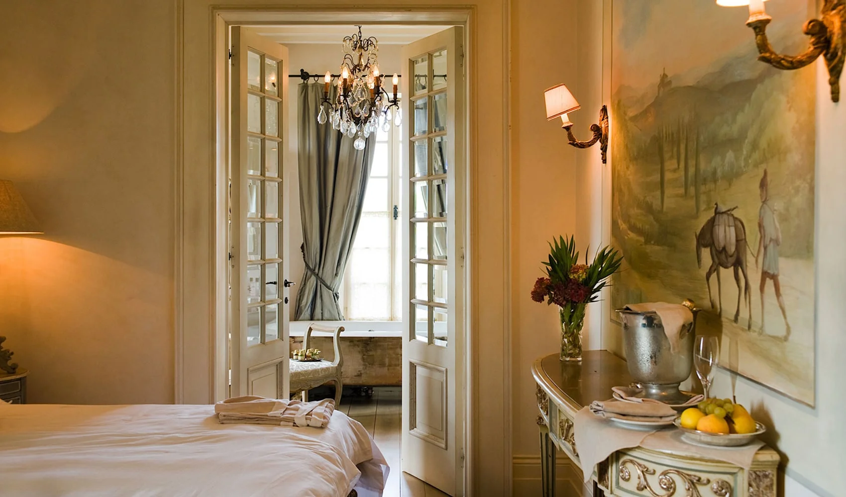 A frescoed villa suite at Borgo Santo Pietro opens to a bathroom with a crystal chandelier and freestanding tub.