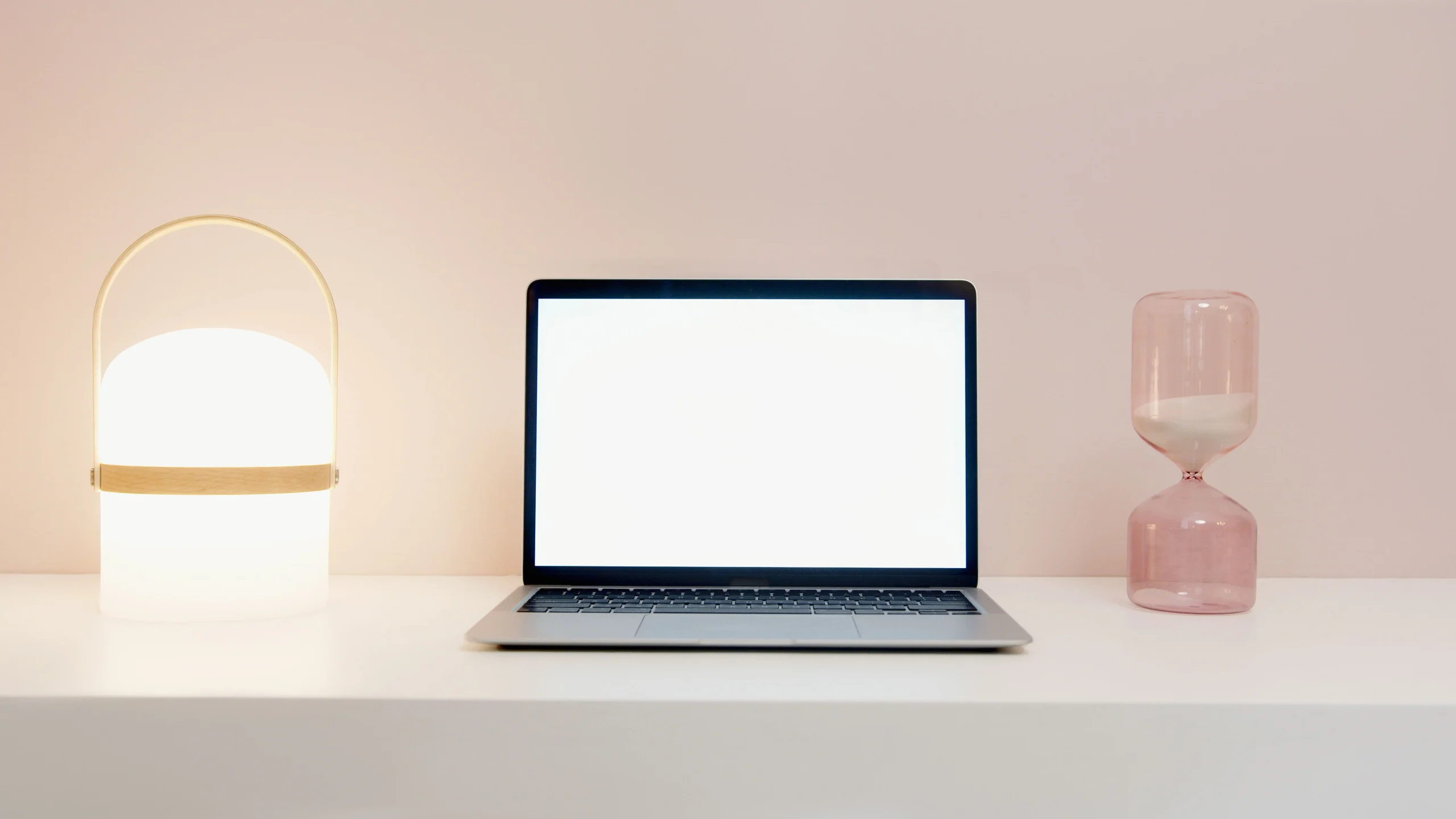Laptop with a blank screen next to an hourglass and a lamp representing digital minimalism.