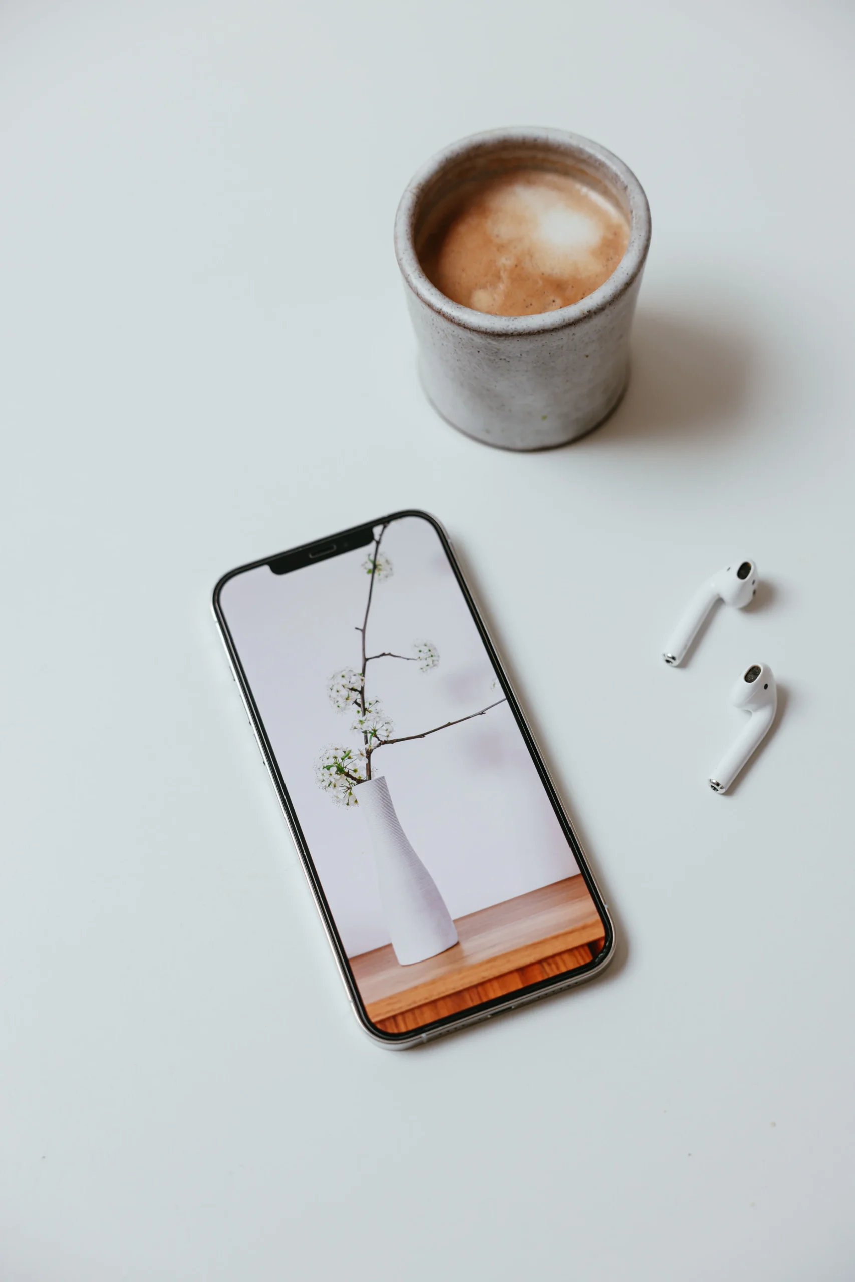 Smartphone displaying a floral wallpaper alongside wireless earbuds and a coffee cup.