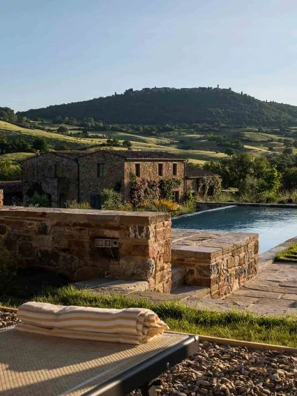 The infinity pool at Follonico, with a striped towel on a lounger and a stone farmhouse and hilltop town beyond.