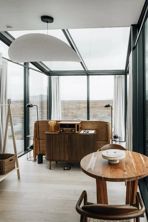A glass-walled cabin interior at Harmony Retreat Lodge, with a walnut table, record player and lava plain views.