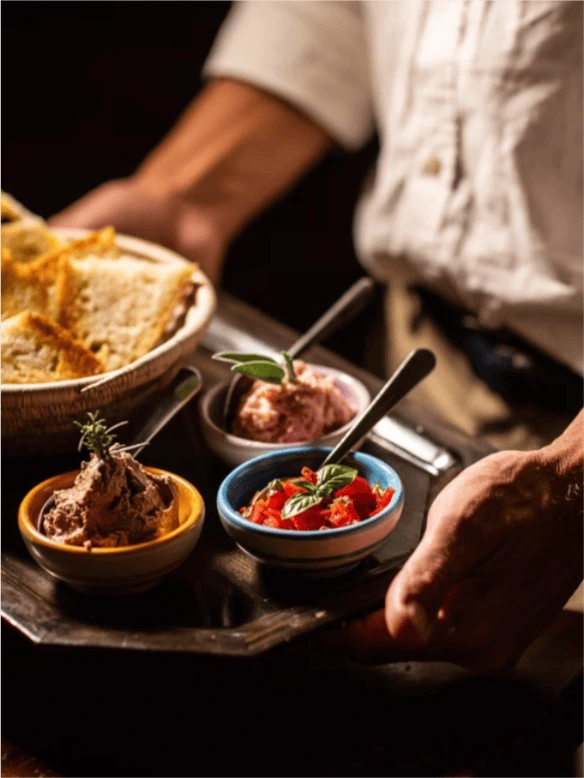 Toasted bread in a woven basket with bowls of chopped tomato and pâté at La Pescaia, garnished with basil and rosemary.