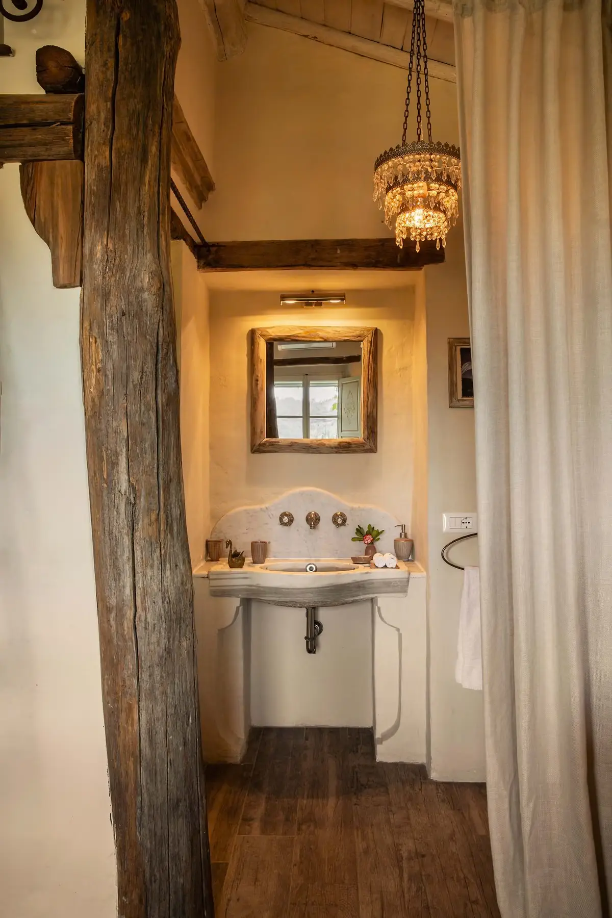 A carved marble washbasin and timber-framed mirror beneath a crystal chandelier in a suite at Lupaia.