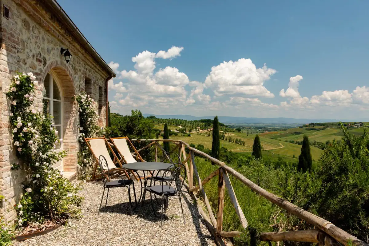 A rose-covered stone terrace at Lupaia with deck chairs and a bistro table, overlooking vineyards and cypress hills.