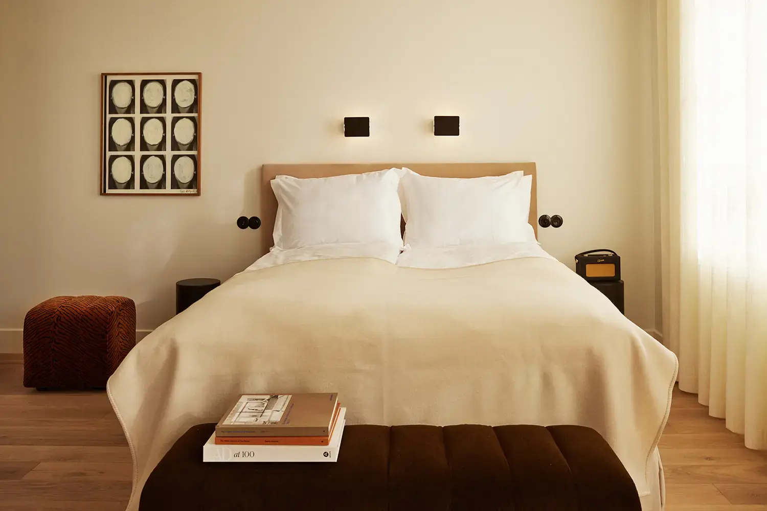 A bedroom at Mjólk hotel, with a cream throw, framed portrait study and velvet bench at the foot of the bed.