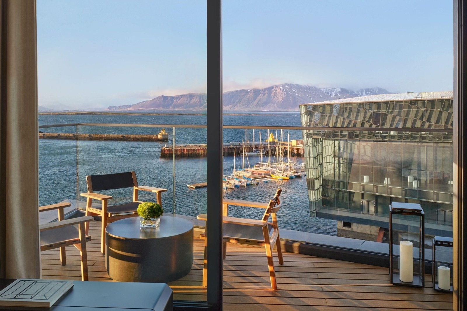 A teak-furnished balcony at The Reykjavik EDITION overlooking the Old Harbor, Harpa concert hall and Mount Esja.
