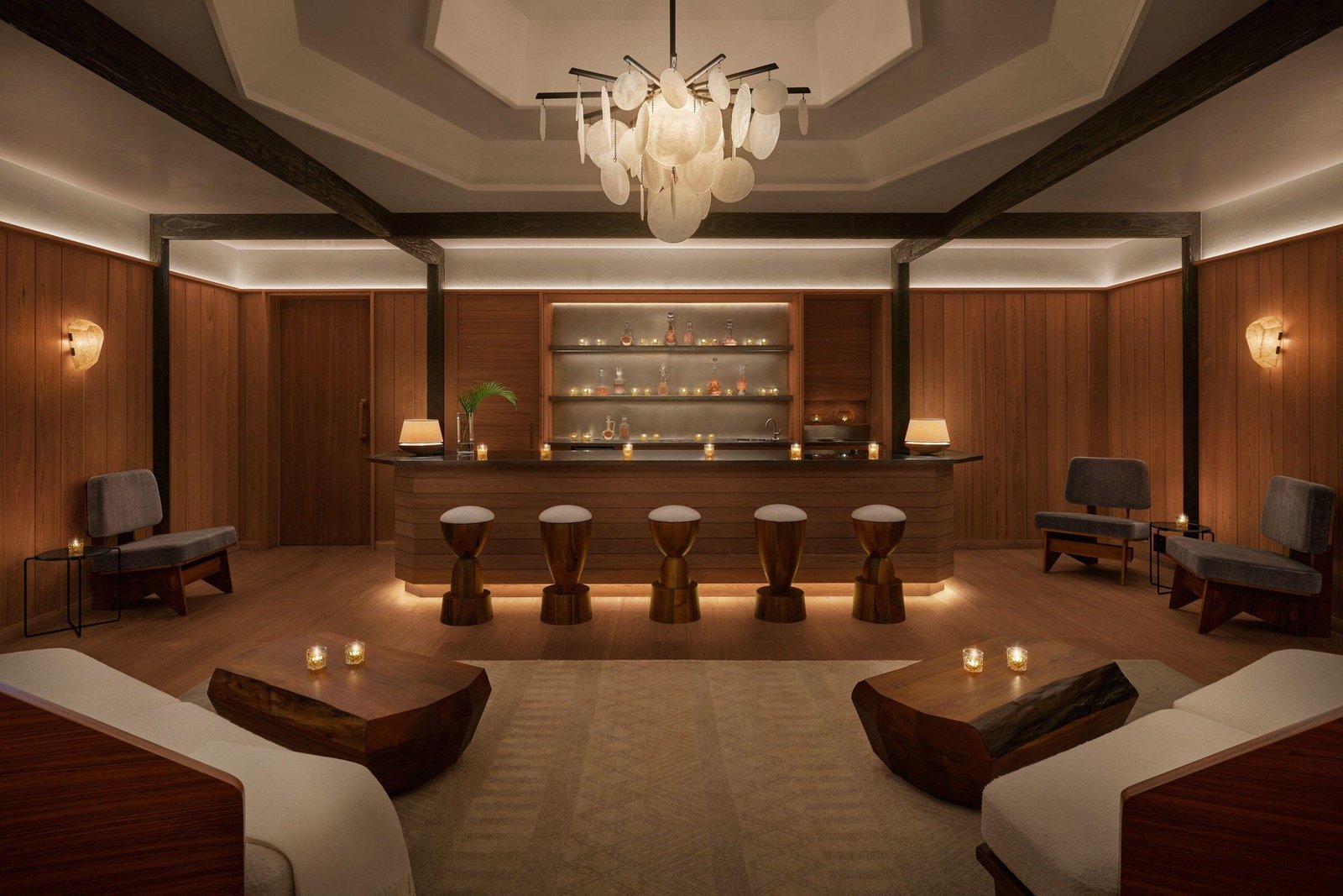 A candlelit lounge at The Reykjavik EDITION, with wood-paneled walls, a shell-disc chandelier and a decanter bar.