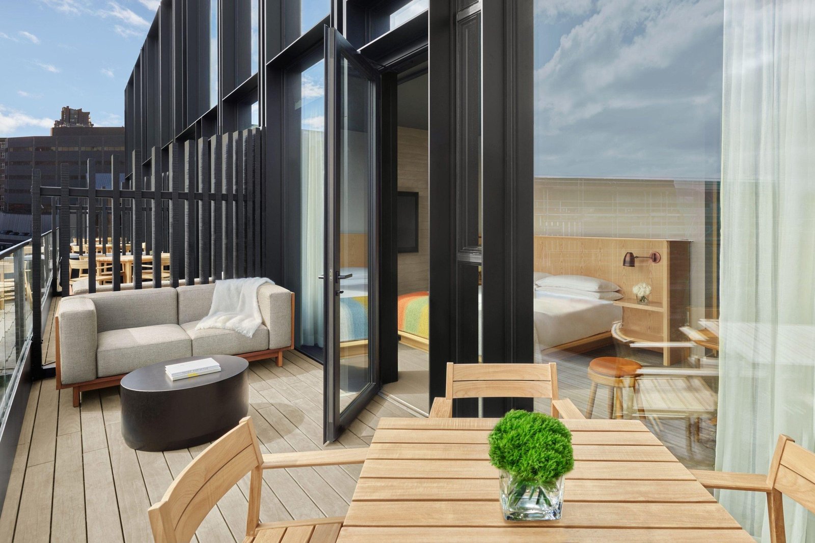 A private terrace at The Reykjavik EDITION, with teak dining chairs and a sofa beside open doors to the bedroom.