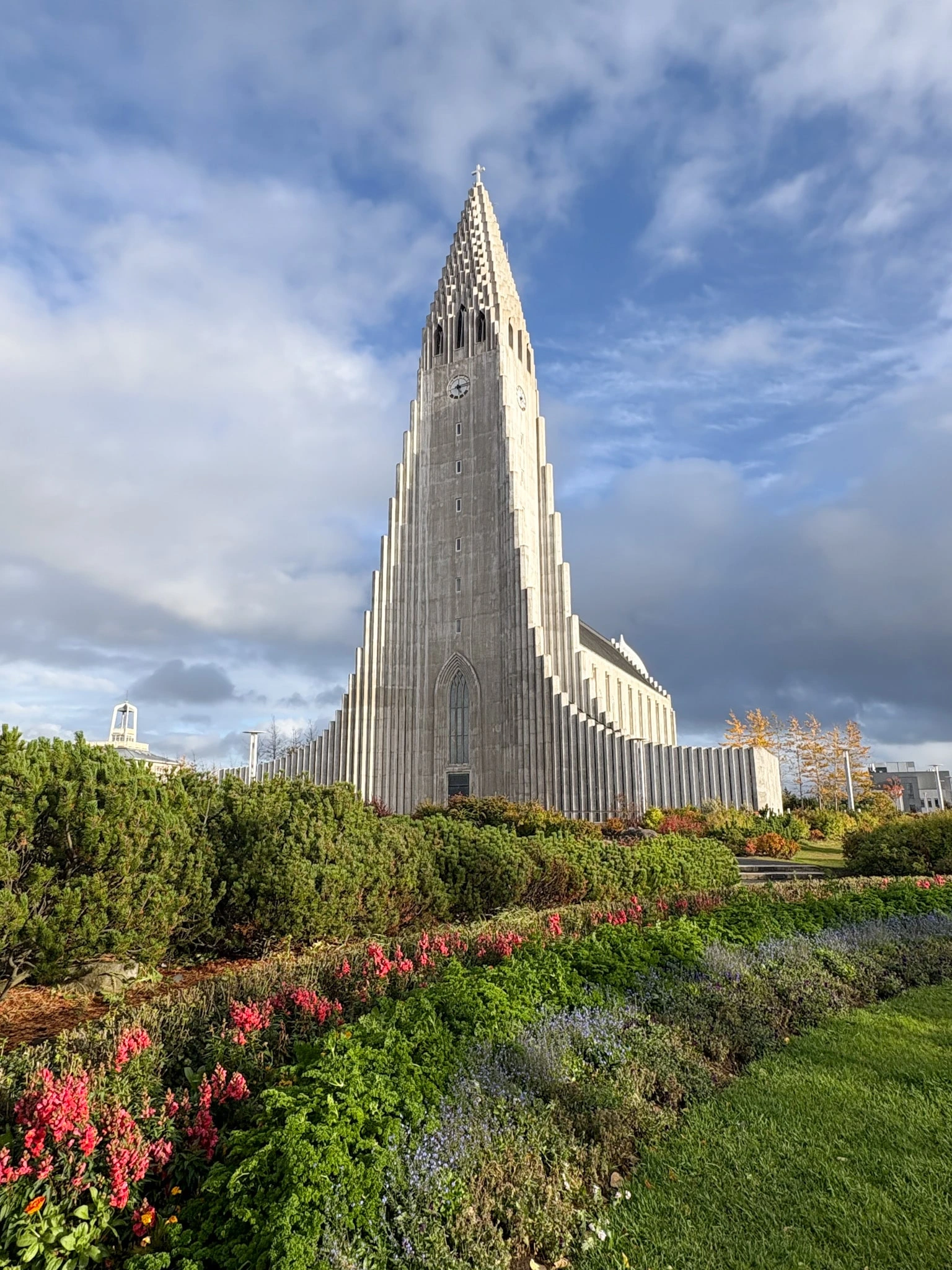 Hallgrímskirkja church rises above a flowering garden in Reykjavik, its basalt-inspired columns against a cloudy sky.