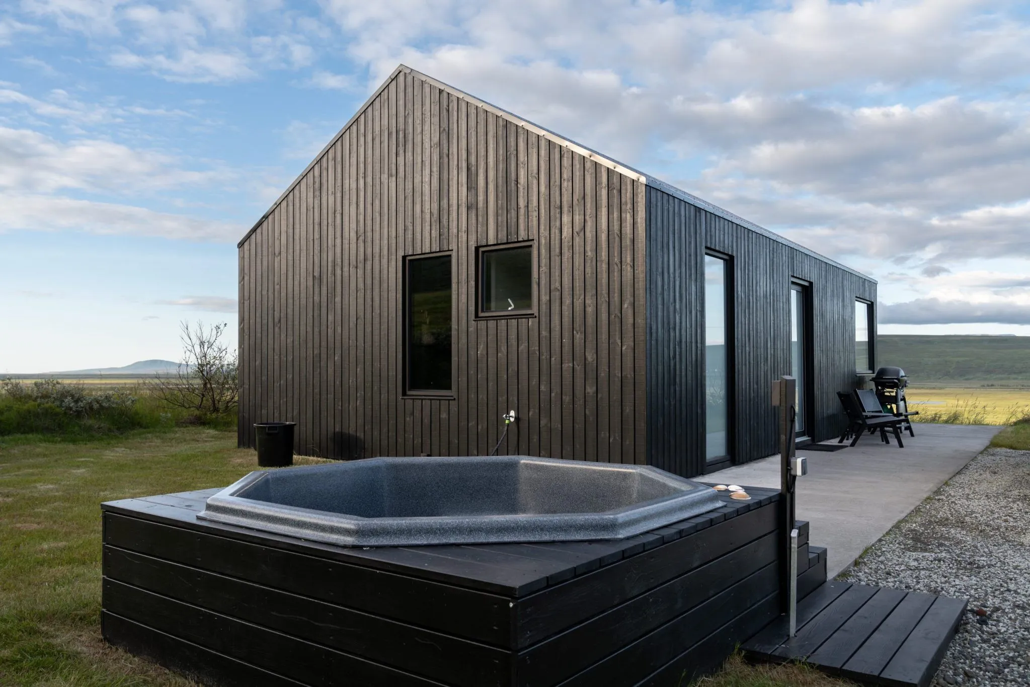 A black timber villa with an outdoor hot tub and terrace at Svartaborg Luxury Villa, open to the Icelandic plains.