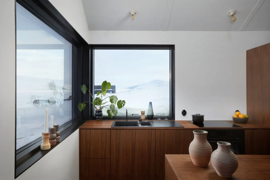 A walnut kitchen with ceramic vases and a corner window onto a snowy landscape at Svartaborg Luxury Villa.